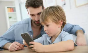 Tata pokazuje synowi jego pierwszy telefon dla dziecka. Chłopiec z zaciekawieniem ogląda ekran.