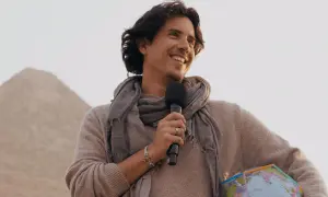 Matias de Stefano, con un micrófono y un globo terráqueo, sonríe ante una pirámide.