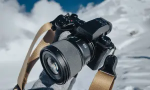 Czarne body aparatu Lumix z obiektywem i beżowym paskiem na tle zaśnieżonych gór.
