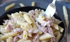 En gaffel lyfter en tugga av krämig skinksås pasta, toppad med riven ost och svartpeppar.