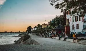 Entspannter Abend am Rhein: Menschen sitzen auf einer Promenade, ein schönes Gebäude und Bäume. Perfekt für Ausflugsziele Wiesbaden.
