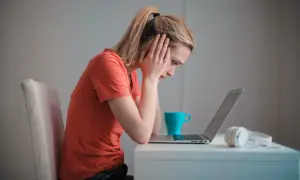 Zmartwiona kobieta przy laptopie, zastanawia się, czy można cofnąć wypowiedzenie. Obok kubek i słuchawki.