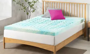 A blue and white memory foam mattress topper with a textured surface sits on a wooden bed frame. Perhaps this is why is my memory foam mattress so uncomfortable.