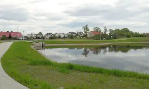 Spokojna okolica w Byszewie Gdańsk. Jezioro z odbiciem chmur, ścieżka i domy w tle.