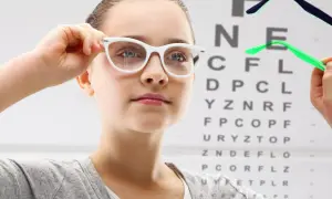 Dziewczynka z wadą wzroku minus 1 przymierza okulary na tle tablicy Snellena.