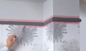 Maintenant, quand enlever bande cache peinture pour une finition parfaite. Un coin de mur avec papier peint à fleurs grises et moulure peinte en gris.