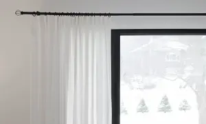 Czarny karnisz z białymi zasłonami na tle okna ze śnieżnym krajobrazem.