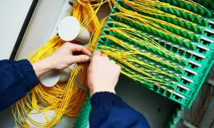 Mains de technicien travaillant sur un panneau de brassage fibre optique, gérant un câble fibre cassé.