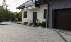 Nowoczesny podjazd z grafitowej kostki brukowej o ciekawych wzorach, prowadzący do domu z garażem.