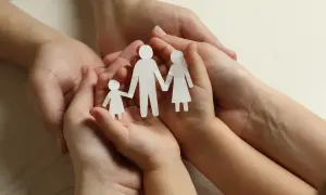 Dłonie dorosłych i dziecka trzymają papierowe figurki rodziny. Symbol wsparcia i troski, jak zasiłek rodzinny.