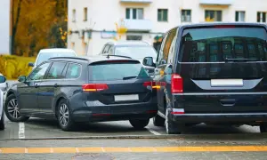 Ciemne kombi i van stoją blisko siebie na parkingu. Widać fragment białego auta. To strefa ruchu, gdzie parkowanie wymaga uwagi.