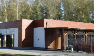 Nowoczesna restauracja Zacisze Ostrzeszów z drewnianą elewacją i przeszklonym wejściem, otoczona drzewami.