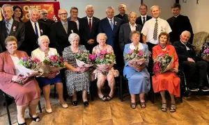 Uroczystość z okazji złotych godów. Seniorzy z bukietami kwiatów świętują 50 lat małżeństwa.