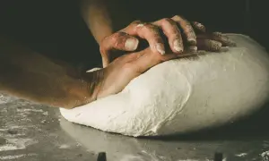Hände kneten den Pizzateig. Die Frage "wie lange pizzateig kneten" beschäftigt jeden Bäcker.