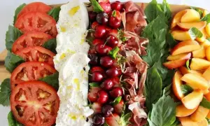 Burrata Antipasti: Tomaten, Burrata, Kirschen, Erdbeeren, Schinken und Pfirsiche auf einem Holzbrett.
