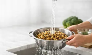 Ceci sono ceci, noti per essere tra i cibi che gonfiano la pancia. Vengono sciacquati sotto l'acqua corrente in una scolapasta.