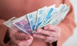 Dłonie trzymają plik polskich banknotów 20, 50 i 100 zł. Czy to wsparcie w ramach bonu senioralnego dla kogoś?