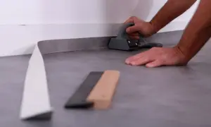 Pose d'un revêtement de sol souple, un rouleau gris est pressé contre le mur avec un outil.
