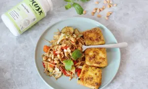 Tallrik med nudlar, grönsaker och friterad tofu. Bredvid en burk HUSK Naturlig fiber, perfekt för mat utan gluten och en balanserad mage.