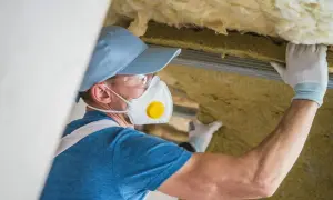 Pracownik w masce i okularach montuje wełnę szklaną, świadomy jej szkodliwości.