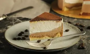 Pyszny sernik z mascarpone, posypany kakao, na talerzu z ziarnami kawy. Obok widelca leży kawałek ciasta.