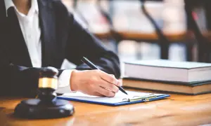 Prawnik pisze dokumenty dotyczące deportacji. Obok leży młotek sędziowski i księgi.