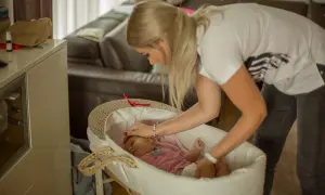 Mama delikatnie kładzie śpiące dziecko do kosza. To pierwszy krok, jak nauczyć dziecko samodzielnego zasypiania.