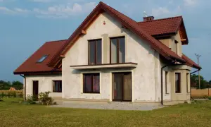 Dom w budowie z brązowym dachem, w tle linia wysokiego napięcia.