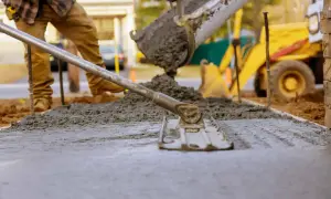 Pracownik wylewa beton, który można lać do temperatury ok. 30°C. W tle koparka.