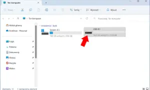 Widok "Ten komputer" z zaznaczonym pendrivem USB (K:). Czerwona strzałka wskazuje na ikonę pendrive'a, sugerując jego szyfrowanie lub przygotowanie do niego.
