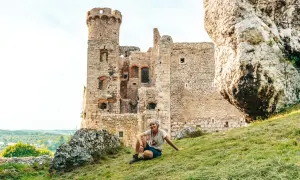 Kobieta odpoczywa na trawiastym zboczu przy ruinach zamku na Szlaku Orlich Gniazd.