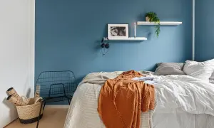 Camera da letto con pareti blu intenso, un letto accogliente con coperte arancioni e bianche, e una sedia in metallo nero. Ottime idee pareti bicolore per un ambiente moderno.