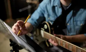 Muzyk w dżinsowej koszuli poprawia nuty, by uchwycić idealny groove. Gitara czeka na swój moment.