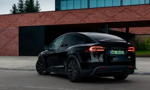Czarna Tesla X z włączonymi światłami z tyłu, zaparkowana przed nowoczesnym budynkiem z cegły.