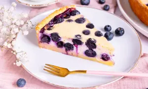 Ein Stück Heidelbeerkuchen Landfrauenart auf einem Teller, garniert mit frischen Heidelbeeren und einer kleinen Gabel.