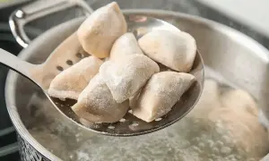 Jak gotować mrożone pierogi? Na łyżce cedzakowej świeżo wyjęte z wrzątku, parujące pierożki.