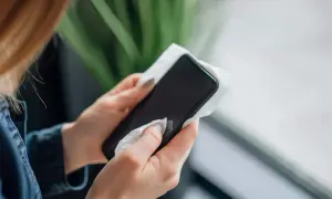 Kobieta dba o higienę, wykonując czyszczenie telefonu wilgotną chusteczką. Dłonie z zadbanymi paznokciami delikatnie przykładają materiał do ekranu.