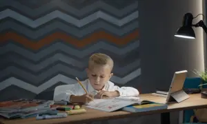 Chłopiec pochyla się nad zeszytem, pisząc ołówkiem. Idealna wysokość biurka dla dziecka zapewnia komfort nauki.