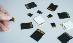 Różne karty pamięci, w tym micro SD, leżą na jasnym tle. Jedna karta jest trzymana w palcach. To jest karta pamięci.