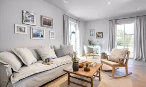 Gemütliches Wohnzimmer in millennial grey mit großem Sofa, Holztisch und Schaukelstuhl. Bilderrahmen zieren die Wand.