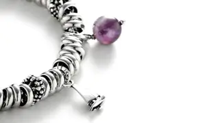 Pulsera de plata con charms, destacando una cuenta de amatista púrpura y un charm en forma de campana.