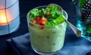 Krämig guacamole med crème fraîche, toppad med färsk koriander och tärnad tomat. Serveras i ett glas med en sked.