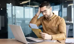 Uomo preoccupato legge una lettera di richiamo per ferie non concordate, con un laptop aperto davanti a sé.