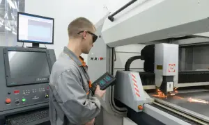 Operator w okularach ochronnych kontroluje proces programowania maszyn CNC za pomocą panelu sterowania.