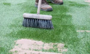 Cepillo extendiendo arena de sílice para césped artificial. Mantenimiento del césped sintético.