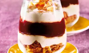 Schichtdessert im Glas mit zerbröselten Amarettini, roter Fruchtsauce und cremiger Masse, garniert mit Mandelblättchen.