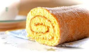 En saftig rulltårta utan bakpulver, pudrad med socker, ligger på en blåvit servett.