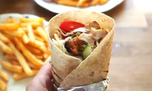 Domowy kebab w tortilli z kurczakiem, warzywami i frytkami w tle.