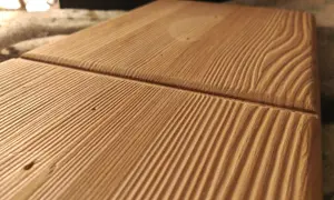 Superficie de madera con surcos paralelos que resaltan las vetas naturales. La luz crea sombras que dan profundidad a la textura.