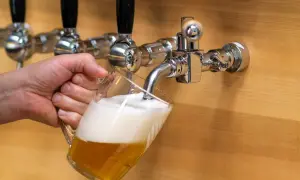 Mano che versa una birra dorata con schiuma abbondante da un rubinetto cromato. La birra alder è pronta da gustare.